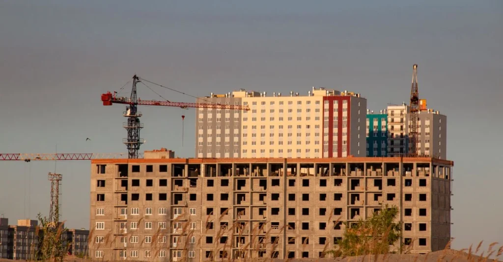 Dźwig precyzyjnie montuje prefabrykowaną ścianę z keramzytu na przygotowanej płycie fundamentowej domu jednorodzinnego.
